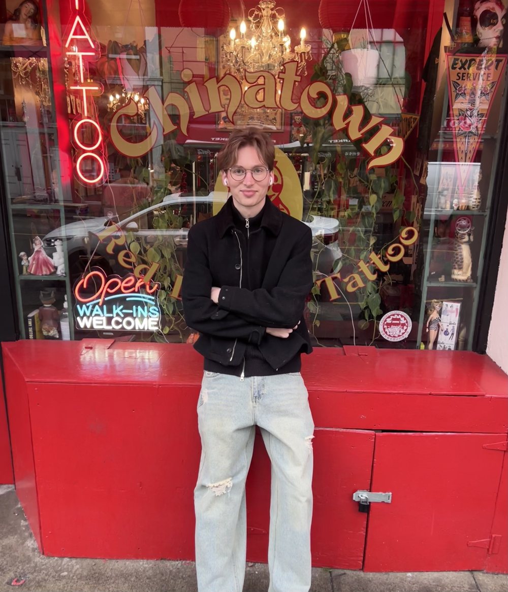 Piercer at Chinatown Piercing standing in front of the studio's red Chinatown storefront on Fisgard Street, Victoria BC